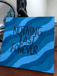 a blue sign that says nothing last forever on top of a wooden table next to a mirror