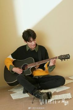 a man sitting on the floor playing an acoustic guitar