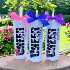 three personalized water bottles with purple and blue bows are sitting on a tree stump