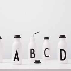 three white bottles with black letters and one has a straw in it