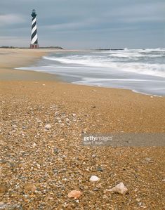 there is a light house on the beach by the water and rocks in the sand