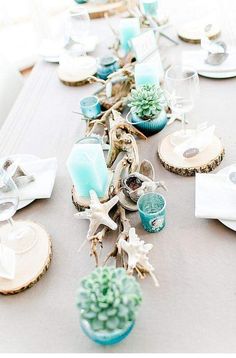 the table is set with dishes, cups and succulents in blue glass vases