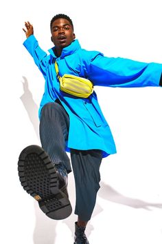 a man in blue jacket and black pants holding a yellow fanny bag while standing on one foot