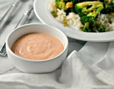 a white plate topped with rice and broccoli next to a bowl of sauce