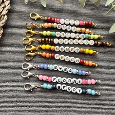 six beaded keychains with name charms on them sitting next to some plants