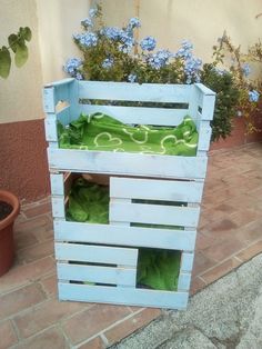 a planter made out of wooden pallets with plants growing inside it and blue flowers in the background