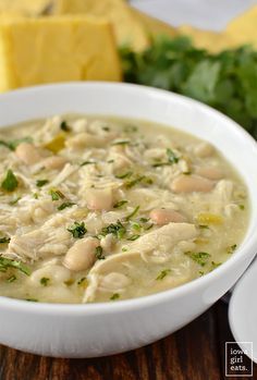 a white bowl filled with chicken and spinach soup on top of a wooden table