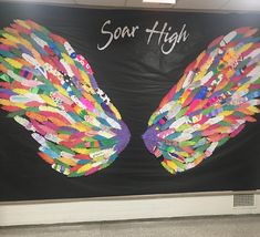 a bulletin board with an angel wing made out of colored crayons and the words soar high on it