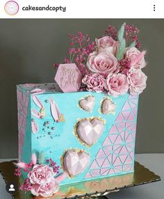 a blue cake with pink flowers and decorations on it's side, in front of a gray background