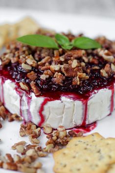 a piece of cheese with blueberry sauce and pecans on top is sitting on a plate next to crackers