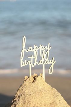 a happy birthday cake topper sitting in the sand