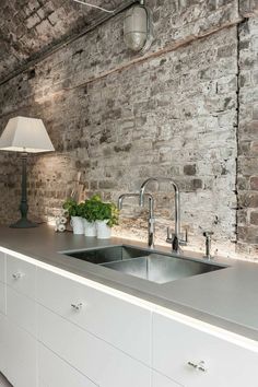 a kitchen with an old brick wall and stainless steel sink in the center, surrounded by white cabinets