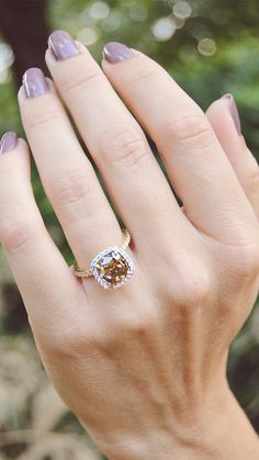 a woman's hand holding a ring with a brown and white diamond in it