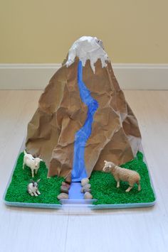 there is a fake mountain with sheep on the grass and water running down it's side