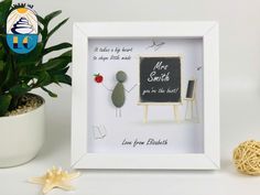 a white frame with a blackboard and some rocks in it next to a potted plant