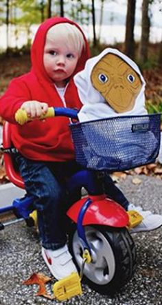 two children in red jackets riding on tricycles and one is holding a stuffed animal