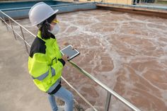 a woman in yellow jacket and white hard hat standing next to railing with brown water