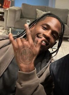 a young man with dreadlocks making the peace sign while sitting in front of a couch