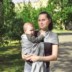 a woman holding a baby wrapped in a grey wrap on her chest and smiling at the camera