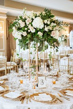 a tall centerpiece with white flowers and greenery sits on top of a table