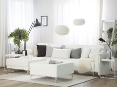 a living room filled with white furniture and lots of plants on the windows sill