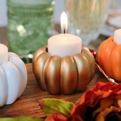 three candles sitting on top of a wooden table next to fall leaves and pumpkins