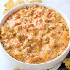 a white bowl filled with chili cheese dip and tortilla chips on the side