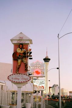 a large sign for a restaurant with a guitar on it's side and a building in the background