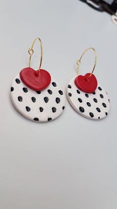 two white and black polka dot earrings with red heart shaped disc dangles on them