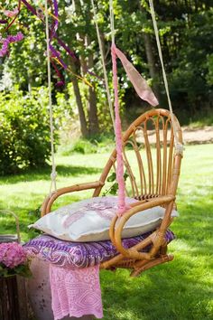 a wicker chair hanging from a tree with pillows on it and flowers in the background