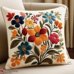 an embroidered pillow with colorful flowers on the front and back of it, sitting on a chair