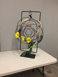 a table topped with a vase filled with yellow flowers next to a metal spiral decoration