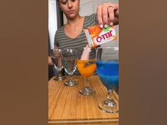 a woman is pouring orange juice into two martini glasses with blue liquid in the middle