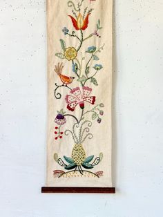 an embroidered wall hanging with birds and flowers on it's side, against a white background