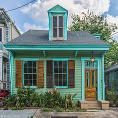 a small green house with shutters on the front and side windows is shown in this photograph