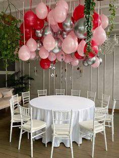 a round table with white chairs and balloons hanging from it's ceiling in a room