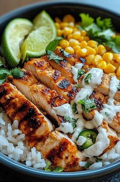 a bowl filled with chicken, rice and corn on top of a table next to lime wedges