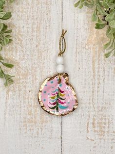 a pink christmas ornament hanging from a wooden table with greenery and white beads