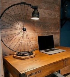 a laptop computer sitting on top of a wooden desk next to a bicycle wheel lamp