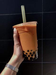 a hand holding up a drink in front of a black tile wall with polka dots on it