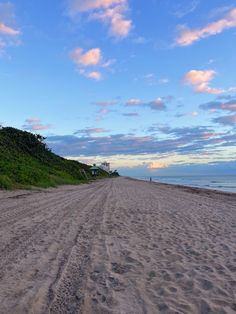 a sandy beach next to the ocean under a blue sky with some clouds in it