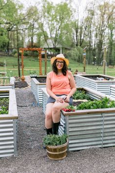 a woman sitting on top of a wooden planter filled with vegetables