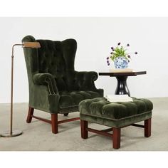 a green velvet chair and footstool in front of a table with a vase on it