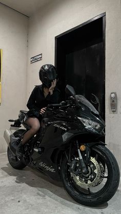 a woman sitting on top of a motorcycle next to a door and talking on a cell phone