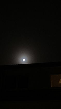 the moon is seen in the dark sky over a building with no lights on it