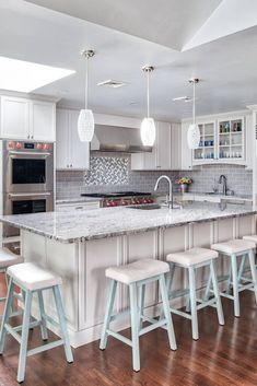 a large kitchen with white cabinets and marble counter tops, along with stools that match the hardwood flooring