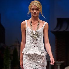 a woman is walking down the runway wearing a white crochet dress and necklace