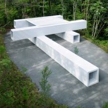 a white bench sitting in the middle of a forest filled with trees and bushes on top of a cement slab