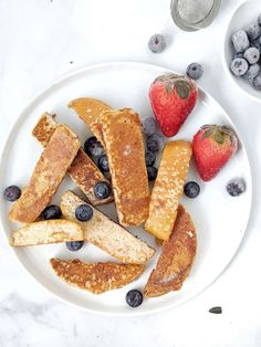 a white plate topped with french toast and blueberries next to strawberries on a table