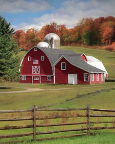 a red barn sits in the middle of an open field with trees and grass around it